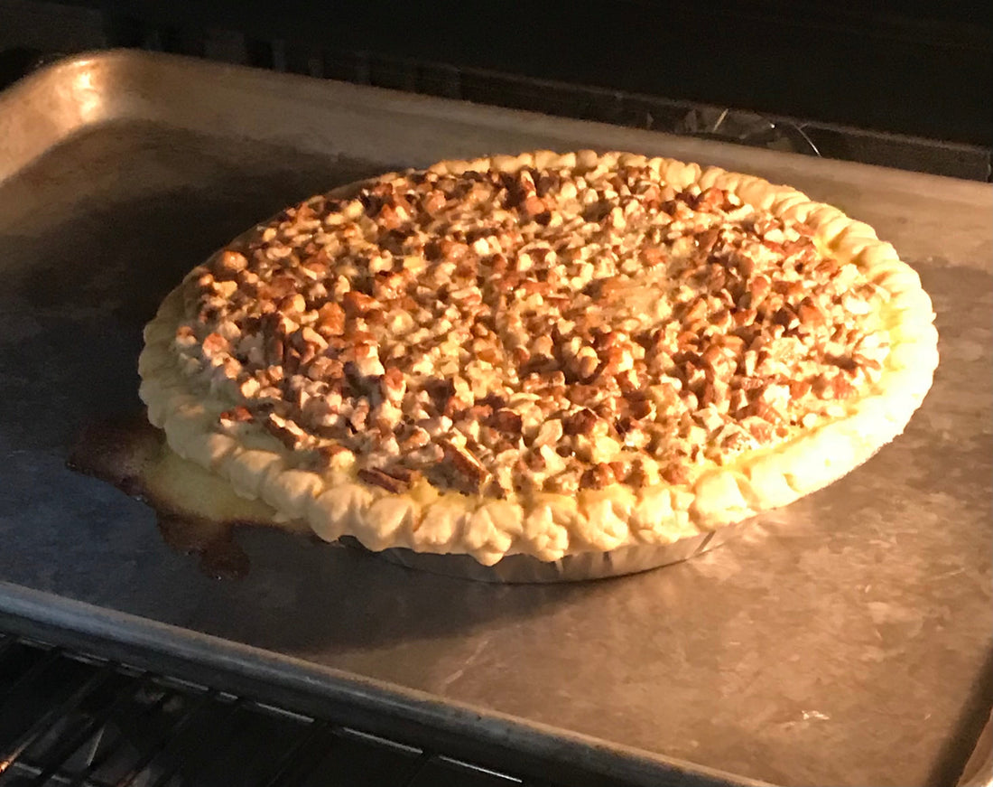 A homemade pecan chess pie baking in the oven on a metal tray, its golden crust and caramelized pecan topping bubbling as it nears perfection