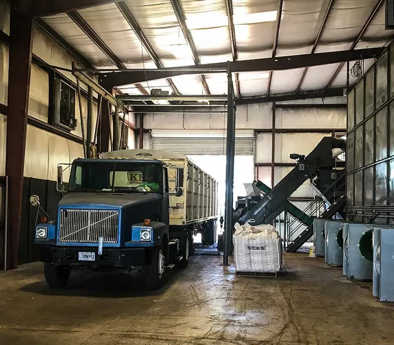 A semi-truck parked inside the Durden Pecan Co. processing facility, ready for loading or unloading pecans beside industrial sorting and cleaning equipment