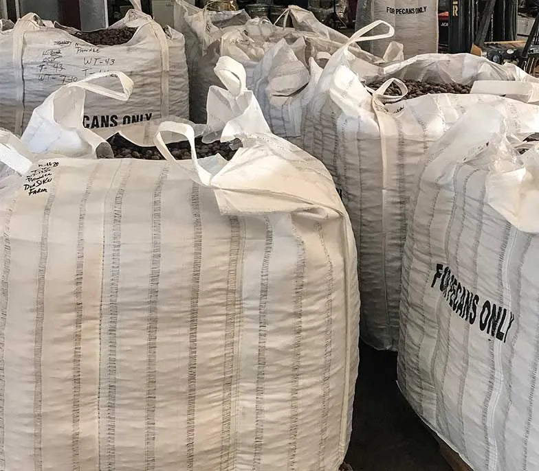 Large white industrial bags labeled “For Pecans Only," filled with freshly harvested pecans inside a processing warehouse